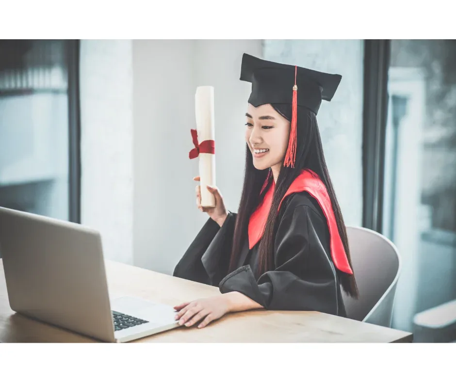 Diploma EaD tem reconhecimento no mercado de trabalho? | Jovem mulher de beca e capelo, segurando um diploma e sorrindo em frente ao computador | UniFaveni