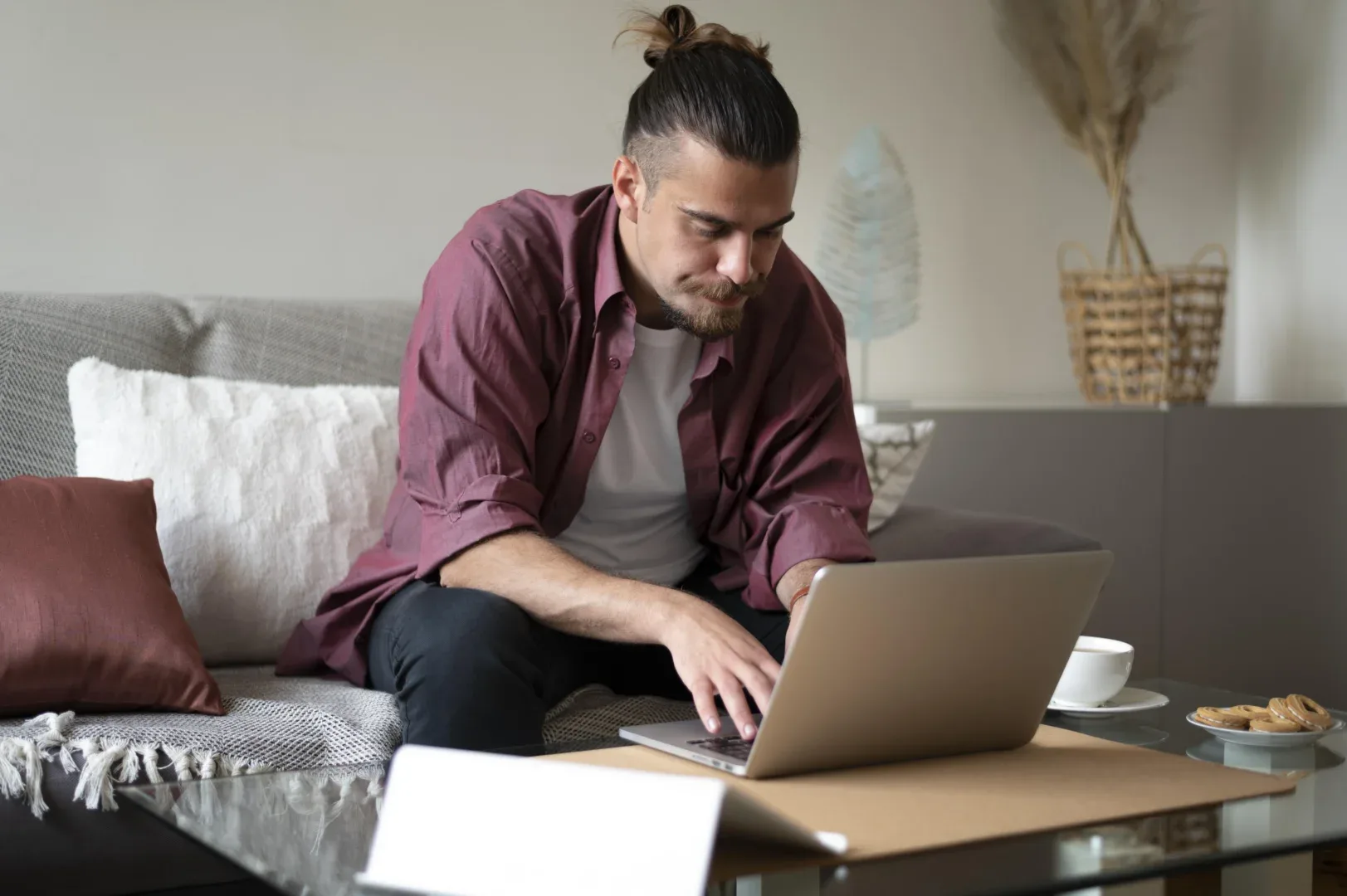 Atividades complementares na graduação EaD: como conseguir? | Jovem homem sentado no sofá mexendo no notebook com uma expressão séria | UNIFAVENI