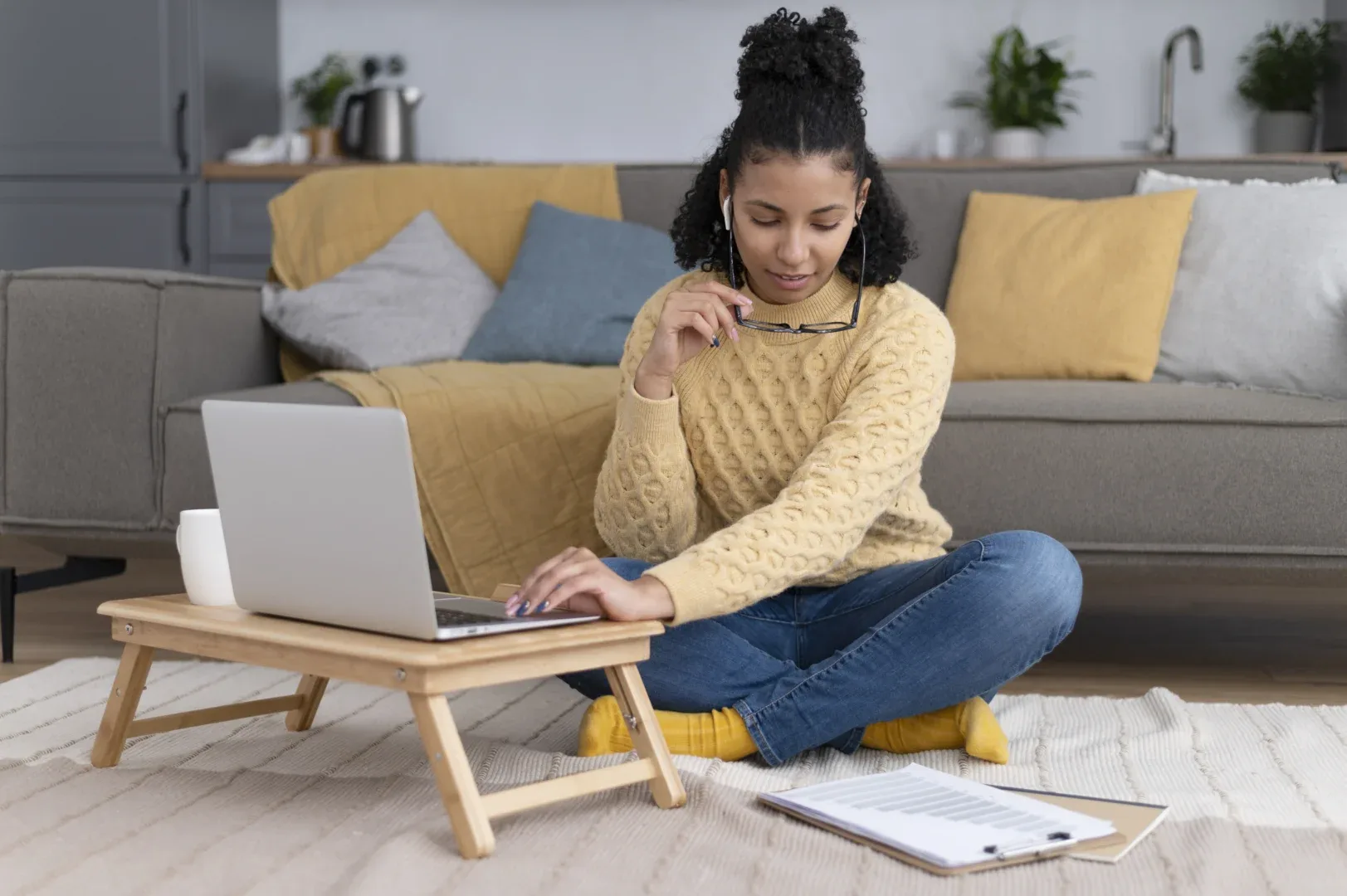 O TCC na graduação EaD é obrigatório? | Foto de jovem sentada no chão da sala com materiais espalhados enquanto mexe no notebook | UNIFAVENI