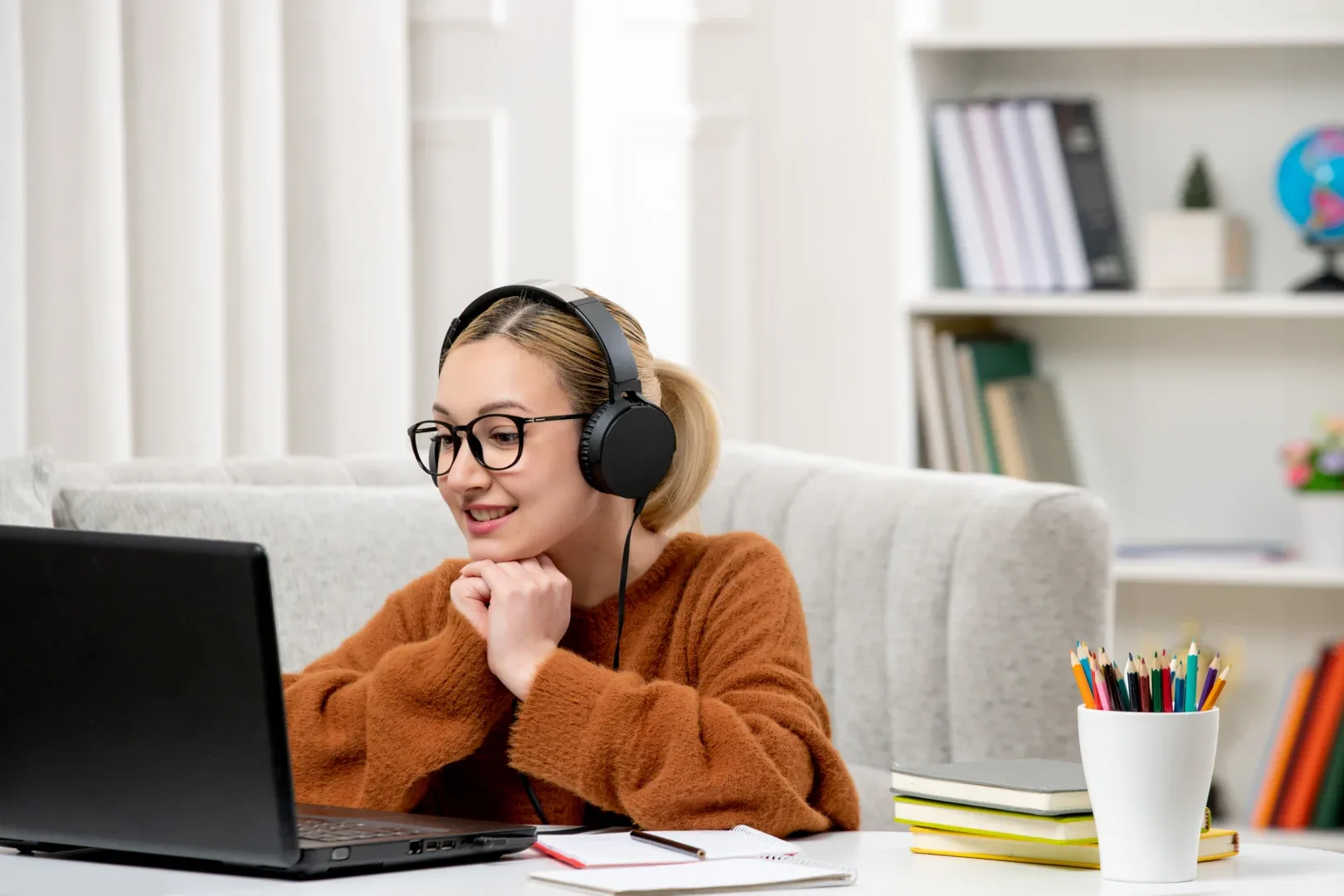 Pegou DP na graduação online? Saiba o que fazer | Foto de jovem garota sentada em uma mesa usando fone de ouvido olhando para o notebook com uma expressão feliz | UNIFAVENI