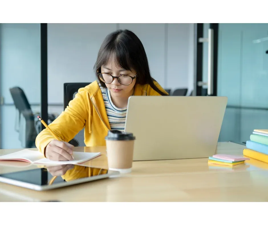 Curso de graduação EaD: o que é preciso para começar? |Jovem mulher fazendo anotações no caderno com notebook na frente | UNIFAVENI