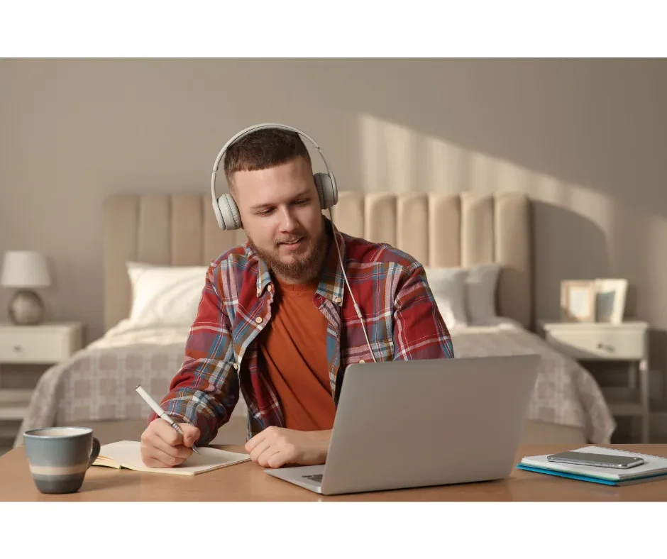 Interações em cursos EaD: como funciona? | Rapaz jovem com fone de ouvido fazendo anotações em frente ao computador | UniFaveni|Interações em cursos EaD: como funciona? | Jovem mulher assistindo uma aula ao vivo online | UniFaveni