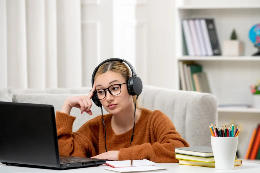 Pegou DP na graduação online? Saiba o que fazer | Foto de jovem garota sentada em uma mesa usando fone de ouvido olhando para o notebook com uma expressão triste | UNIFAVENI|Pegou DP na graduação online? Saiba o que fazer | Foto de jovem garota sentada em uma mesa usando fone de ouvido olhando para o notebook com uma expressão feliz | UNIFAVENI
